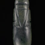A dark-green, capsule-shaped jadeite pendant with an abstract face and line carvings.