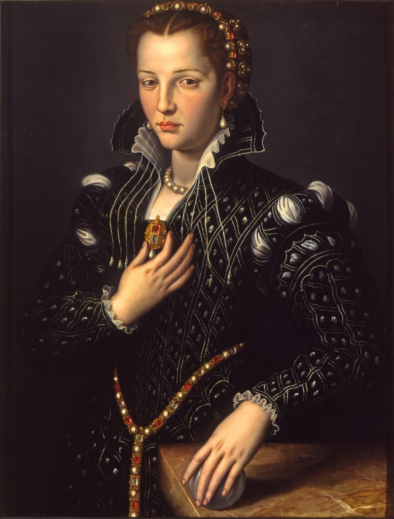 An oil painting of a woman wearing a black dress adorned with jewels and holding a gold pendant in her right hand. The background is dark gray, and there is a wooden table in the foreground, in the bottom right corner.