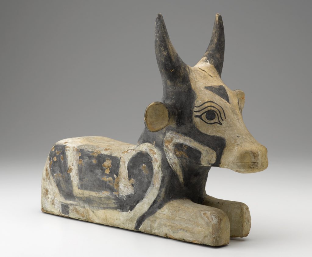 A wooden sculpture of a seated, black-and-white painted bull.
