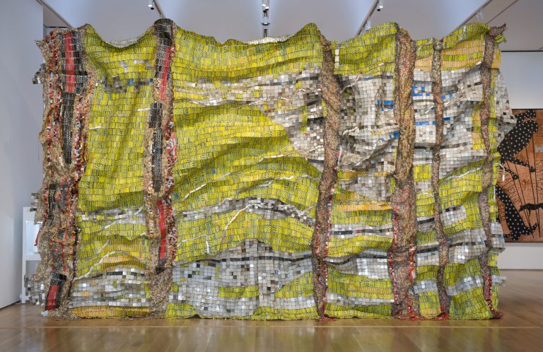 Large mixed media sculpture made of multicolored metal pieces connected together to resemble crumpled aluminum foil, displayed horizontally.