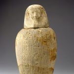 Una jarra de piedra con tallas jeroglíficas y una tapa con un rostro humano.