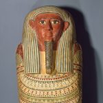 Un ataúd de madera con forma de cuerpo humano, con símbolos y deidades del antiguo Egipto pintados en su superficie.