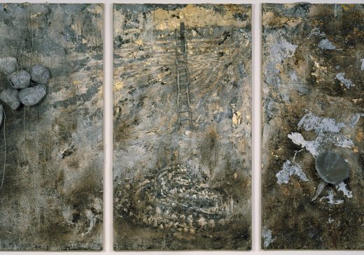 A three-panel abstract painting in shades of gray, brown, and gold. The panel on the left has several rocks attached to it. The middle panel has a small ladder attached to it, with a painted surface below. The panel on the right has a silver funnel-shaped object attached to it.