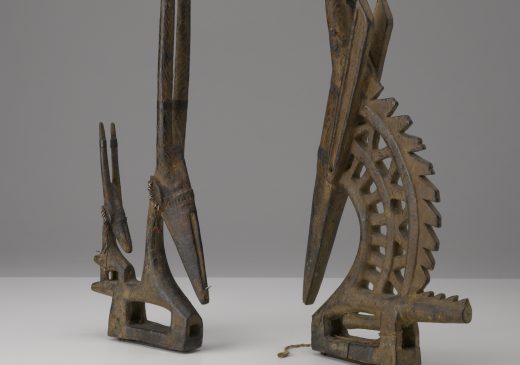 A sculpted wooden pair of male and female headdresses with tall, horned antelope heads and short, stout aardvark bodies.