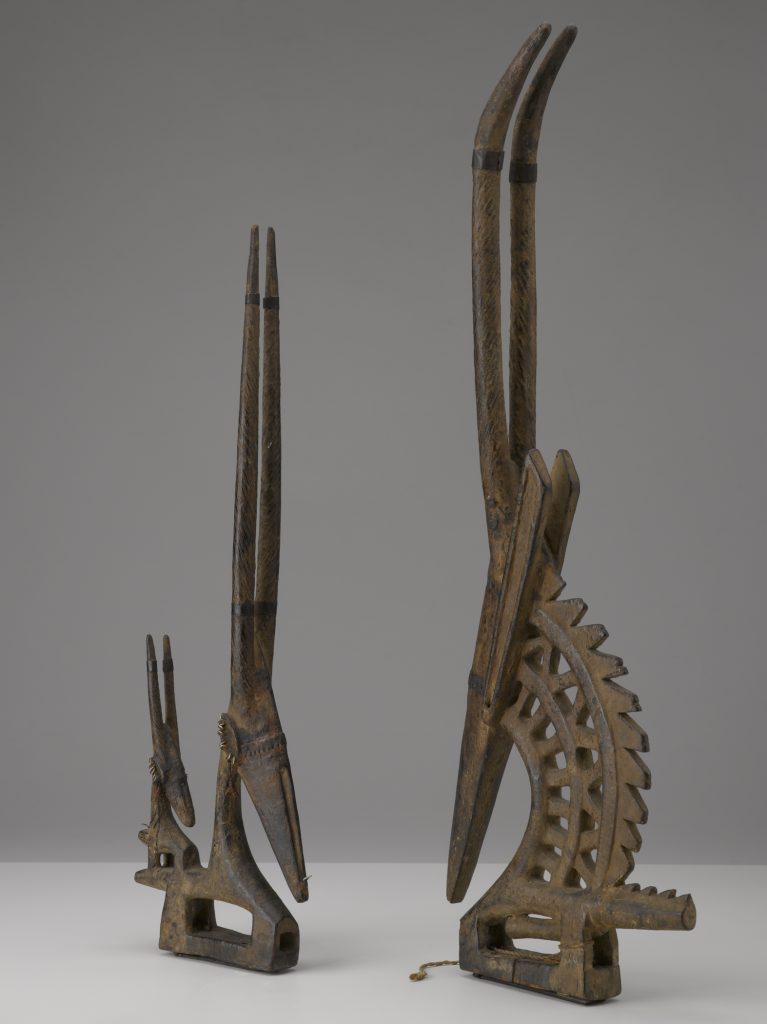 A sculpted wooden pair of male and female headdresses with tall, horned antelope heads and short, stout aardvark bodies.