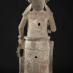 Back view of a ceramic sculpture of a female holding a torch in her right hand and a bag in her left hand.