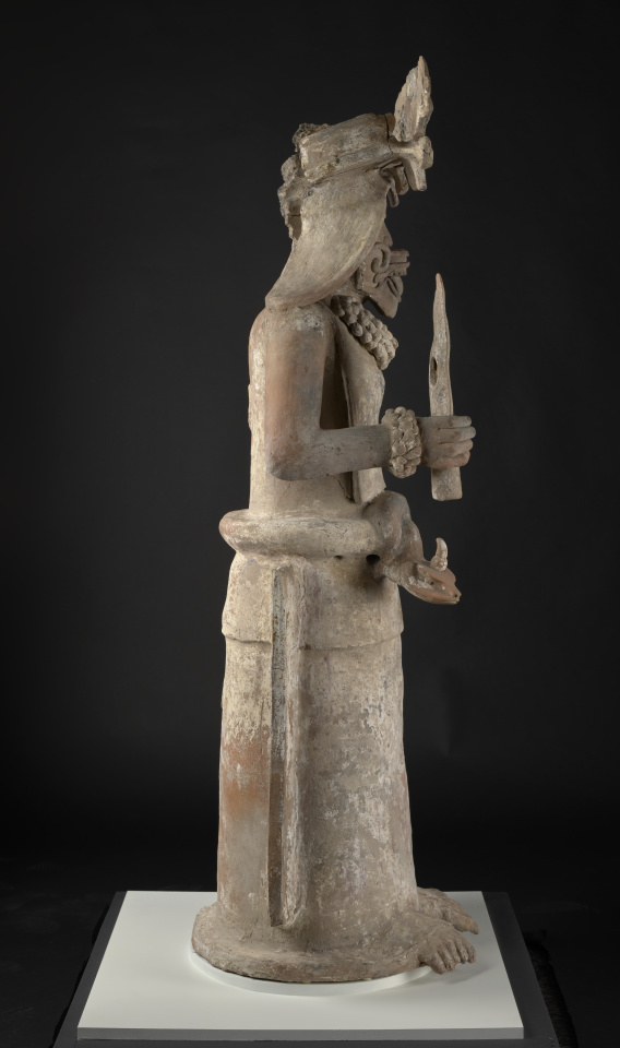 A sculpture of a female deity holding a torch in her right hand and a bag in her left hand.