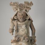Escultura de una deidad femenina que sostiene una antorcha en la mano derecha y una bolsa en la izquierda.