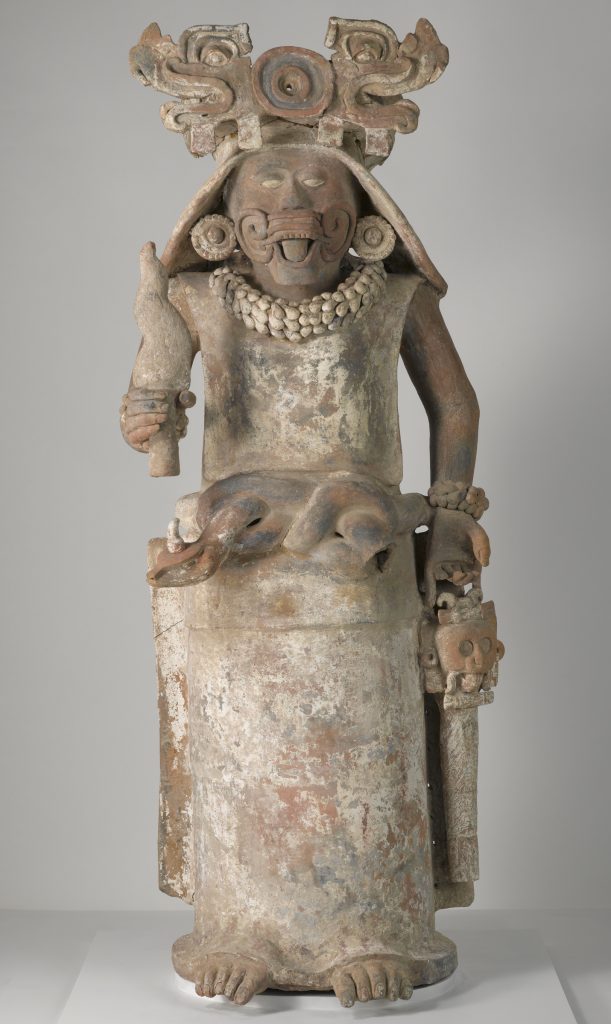A sculpture of a female deity holding a torch in her right hand and a bag in her left hand.