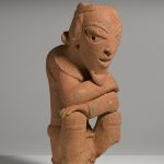 Escultura de cerámica de una figura masculina arrodillada con los brazos cruzados.