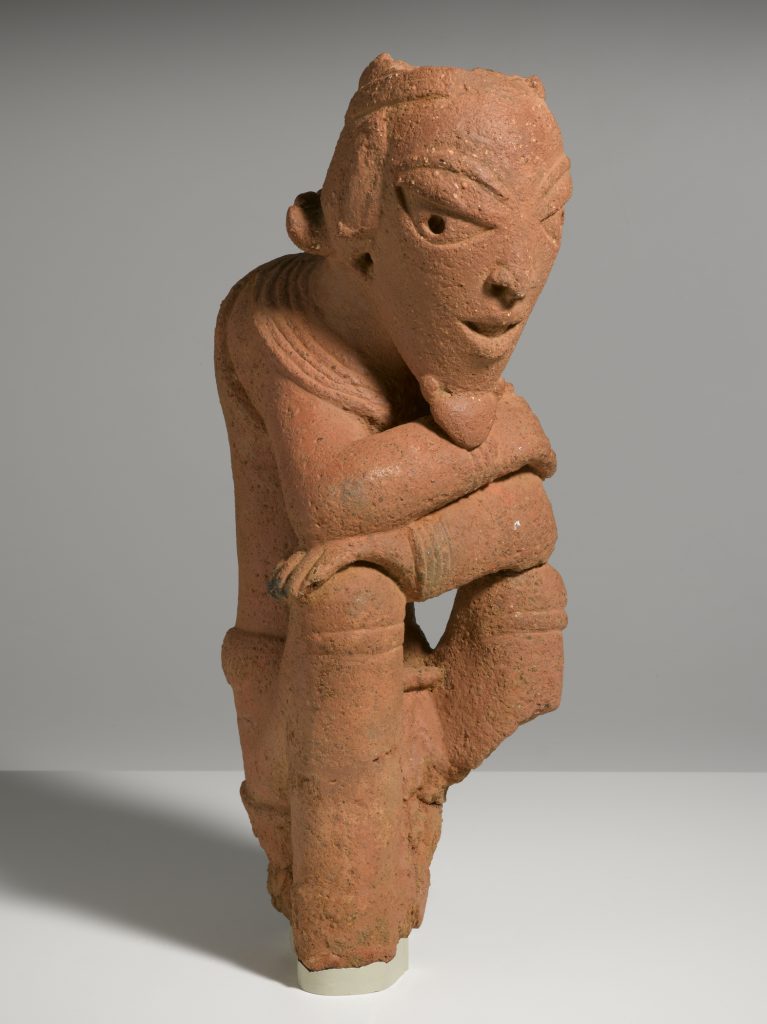 A ceramic sculpture of a kneeling male figure with crossed arms.