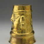 Side view of a gold cup positioned upside down, decorated with human facial features.