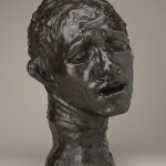 A bronze sculpture of a man’s head that is tilted to one side. He is looking down, with his eyes nearly closed and his mouth slightly open. His pained facial expression makes him appear to be in distress.
