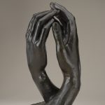 A bronze sculpture of two right hands reaching toward one another, with the fingertips just touching.