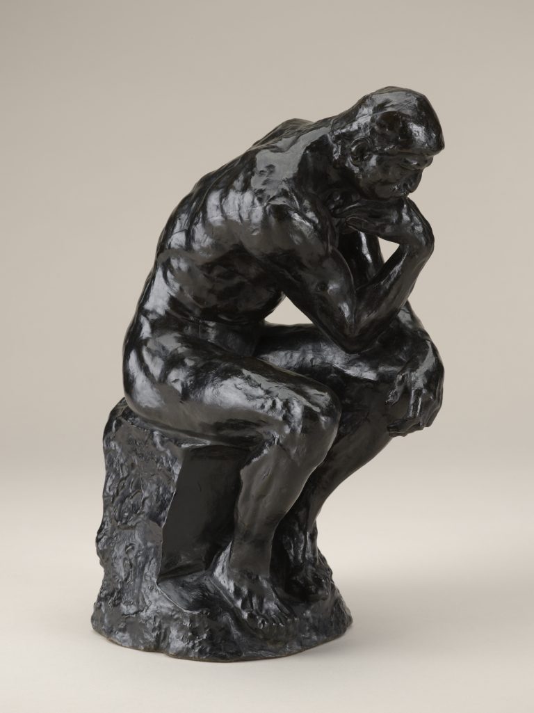 A bronze sculpture of nude male figure seated on a rock, propping his face on his hand and appearing to be deep in thought.