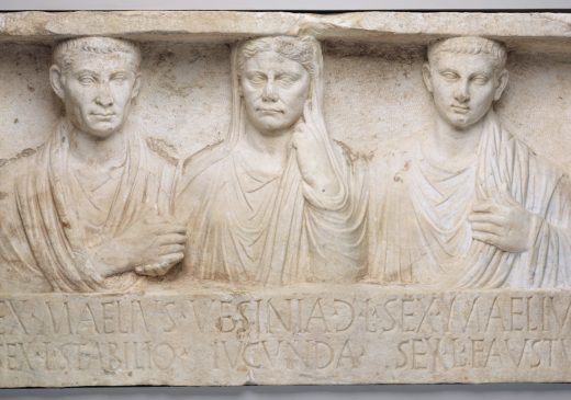 A rectangular, sculpted white marble monument depicting three human figures: a husband and wife and their son. Their names are inscribed in Latin at the bottom.