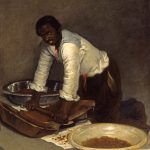 A painting of a dark-skinned man in a white shirt kneeling and looking directly at the viewer. He grinds cacao with a roller on a flat, heated stone. There are large bowls of ground cacao to his right and left. Patties of prepared chocolate rest on paper in the foreground.