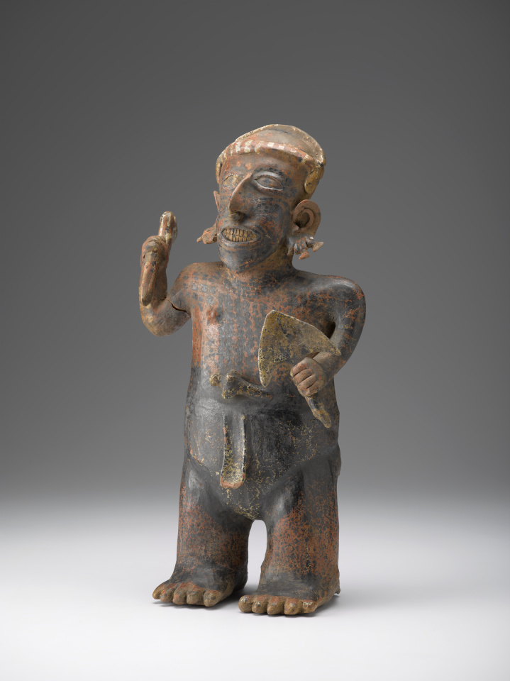Figura de cerámica de un hombre que sostiene una espada en una mano y un objeto parecido a un pájaro en la otra.