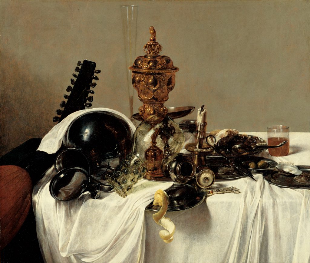 An oil painting of a table with a white tablecloth in front of a plain wall. The table is scattered with food and drinks. Two containers, made of pewter and glass, are overturned near the edge of the table. A gold centerpiece and a tall flute glass tower over the objects in the center of the painting. The neck of a lute leans against the table.