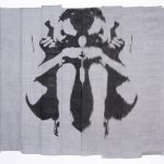 A piece of gray cloth with an almost symmetrical black inkblot design in the middle.