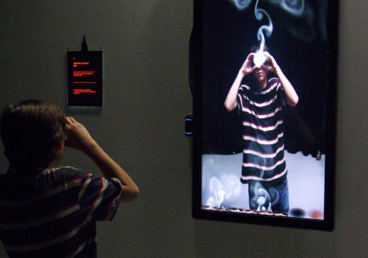Una imagen de un gran televisor vertical que muestra un vídeo del espectador con humo blanco saliendo de sus ojos.