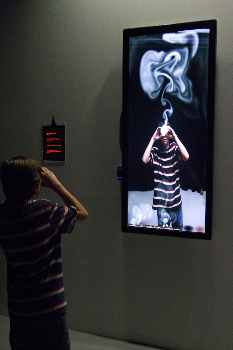 The Year’s Midnight (Shadow Box 5) An image of a large vertical TV that shows a video of the viewer with white smoke coming out of their eyes.