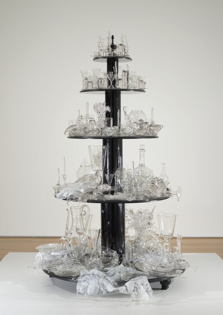 Sculpture made of five round wooden tiers painted black; each holds glass objects ranging from completely intact to broken and shattered.