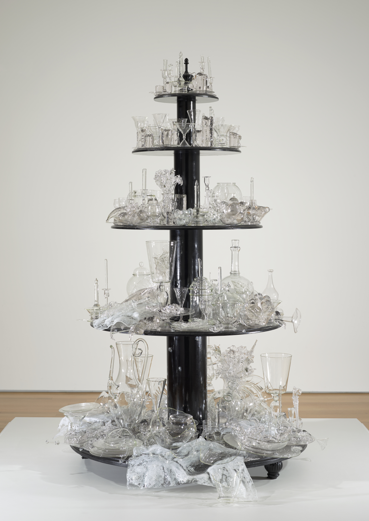 Bride Sculpture made of five round wooden tiers painted black; each holds glass objects ranging from completely intact to broken and shattered.