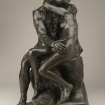 A bronze sculpture of a seated nude male and female figure who are embracing one another as they kiss.