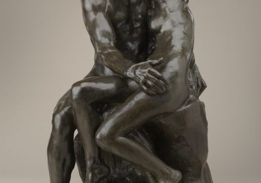A bronze sculpture of a seated nude male and female figure who are embracing one another as they kiss.