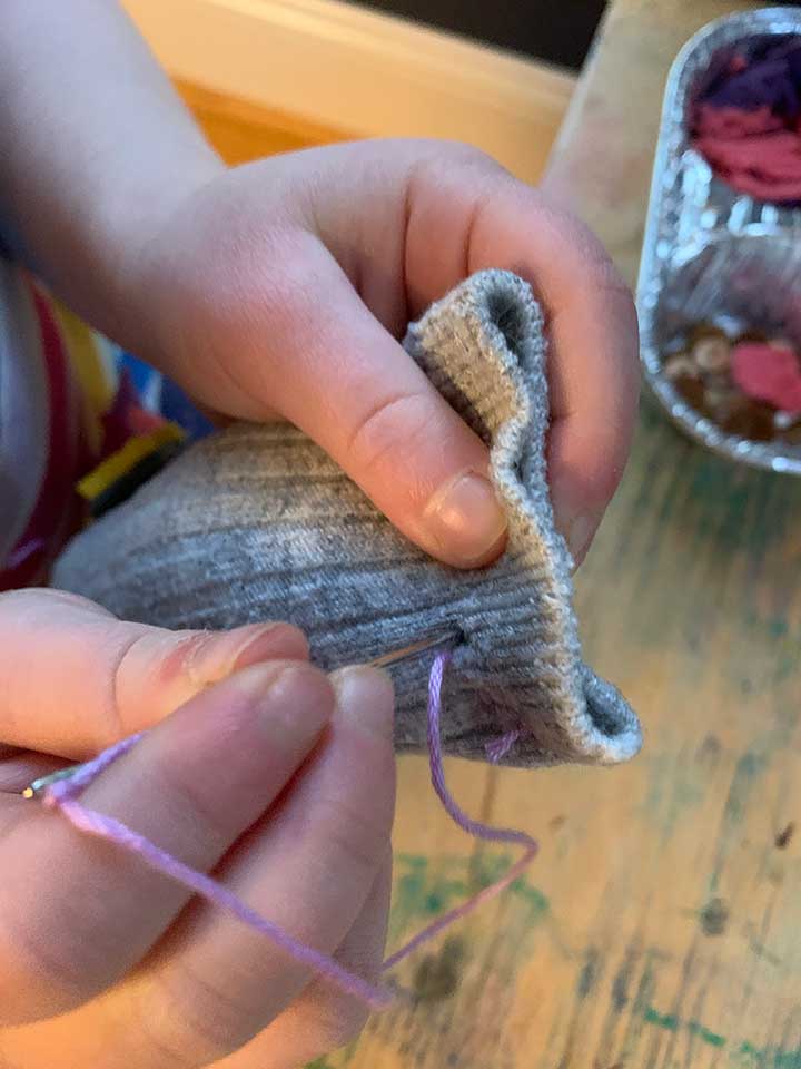 El niño sostiene un calcetín en la mano con una aguja para empezar a crear un softy.
