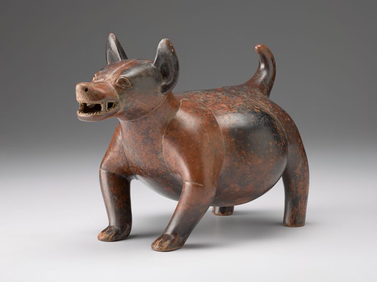 A reddish-brown ceramic sculpture shaped like a dog with pointed ears, open mouth, round belly, and curled tail, standing on four legs.