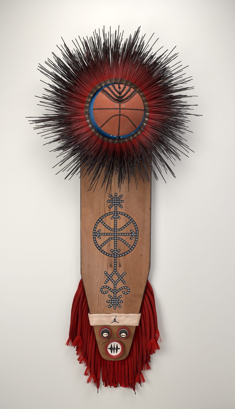 A mixed-media sculpture made of a wooden ironing board, cowrie shells, braided synthetic hair, shoe laces, clay pots, and a basketball.