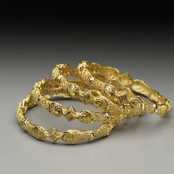 Cuatro pulseras bañadas en oro apiladas unas sobre otras e inclinadas hacia la derecha