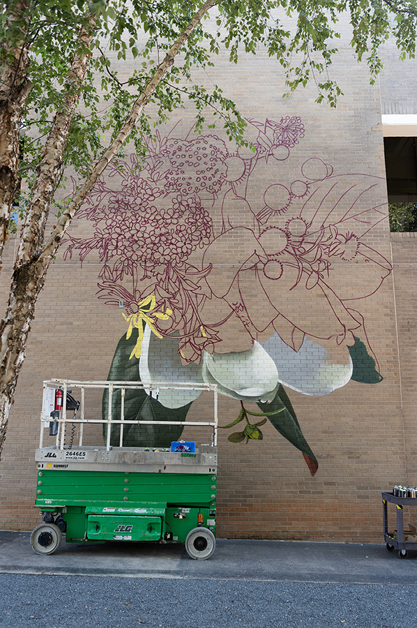 A large-scale mural of white, yellow, and pink flowers painted on a brick building.
