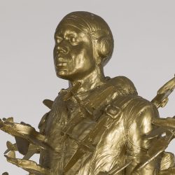 Side view of the top portion of a gold colored sculpture of a Tuskegee airman pierced by small airplanes