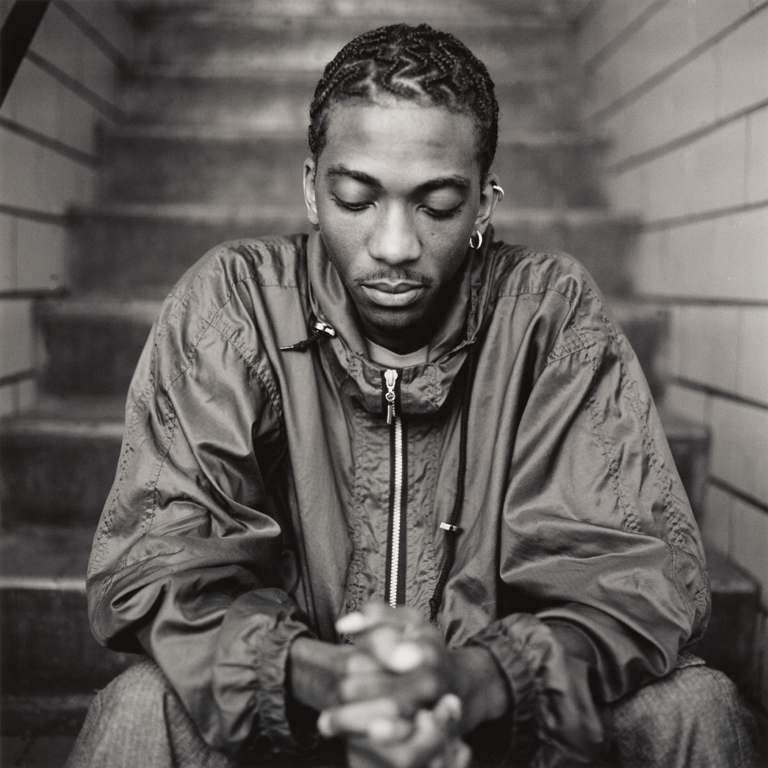 a young Black man sits on stairs with his hands clasped