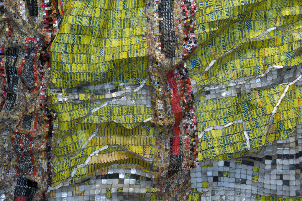 Una gigantesca escultura metálica en forma de tela con secciones amarillas y grises plateadas separadas por líneas verticales multicolores.
