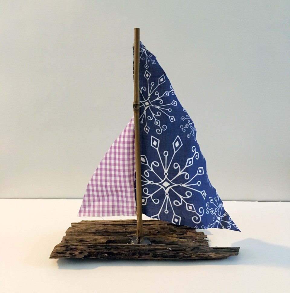 A boat made from found wood with a blue and purple fabric sail.