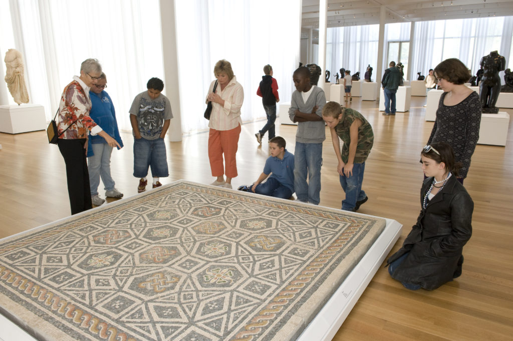 Un mosaico romano con motivos florales y geométricos realizado con piezas de mármol blanco y vidrio de color.