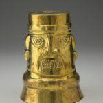 A gold cup decorated with the face of a Peruvian god.