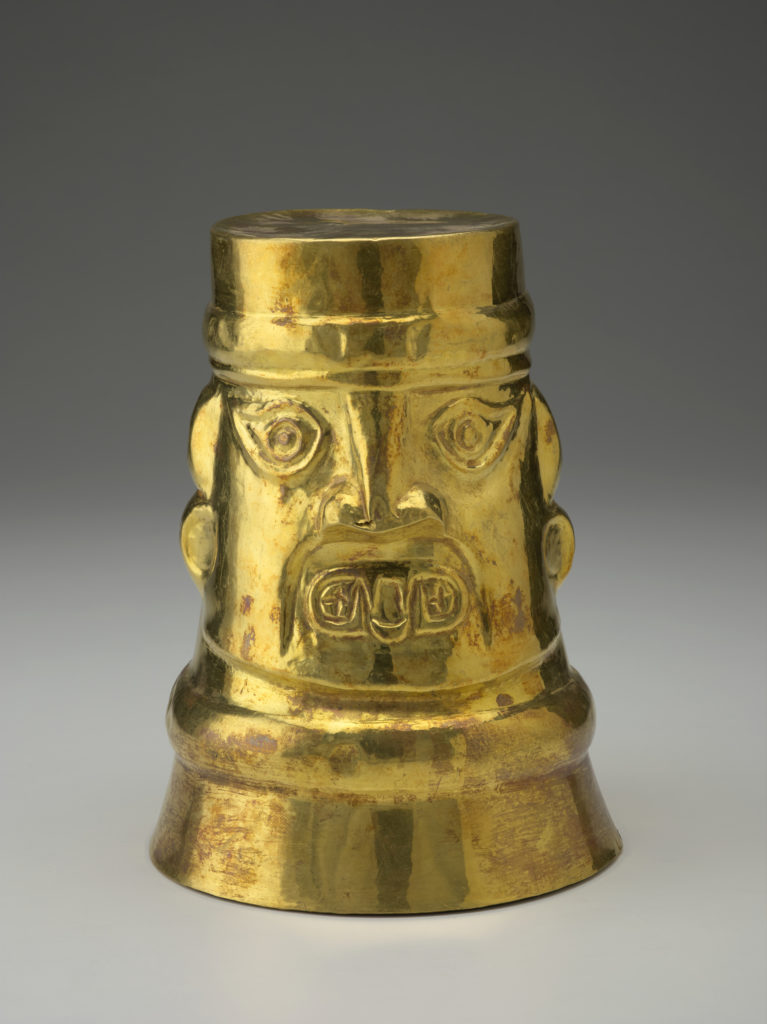 A gold cup decorated with the face of a Peruvian god.