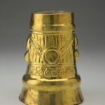 Back view of a gold cup positioned upside down, decorated with human facial features.