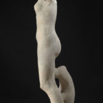 A marble statue of a nude goddess figure, missing both arms, with a dolphin figure at her feet. Side view.