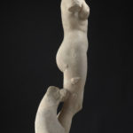 A marble statue of a nude goddess figure, missing both arms, with a dolphin figure at her feet. Side view.