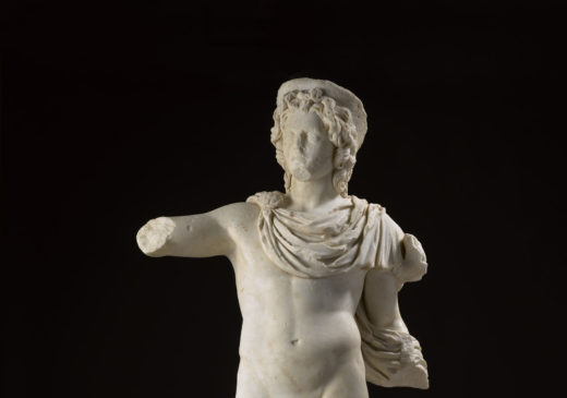A marble statue of the Greek sun god Helios, without arms, depicted wearing only a short cloak over one shoulder and a partial crown, with the head of a horse at his feet.
