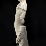 A marble statue of the Greek sun god Helios, without arms, depicted wearing only a short cloak over one shoulder and a partial crown, with the head of a horse at his feet. Side view.