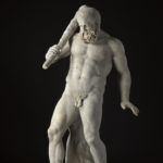 Escultura de mármol blanco de una figura masculina desnuda y con barba que sostiene un garrote sobre el hombro. Su peso es soportado por un tronco de árbol detrás de él.