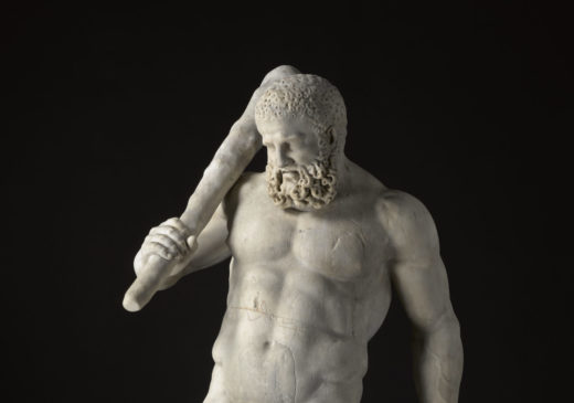 Escultura de mármol blanco de una figura masculina desnuda y con barba que sostiene un garrote sobre el hombro. Su peso es soportado por un tronco de árbol detrás de él.