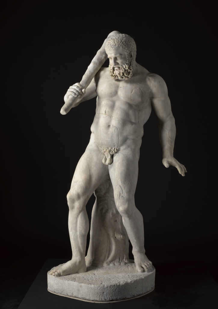 A white marble sculpture of a nude, bearded male figure holding a club over his shoulder. His weight is supported by a tree trunk behind him.